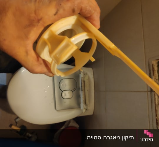 יד מחזיקה חלק פלסטיק ליד אסלה עם כפתור הדחה
